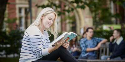 一名学生读一本书在校园内坐在户外。
